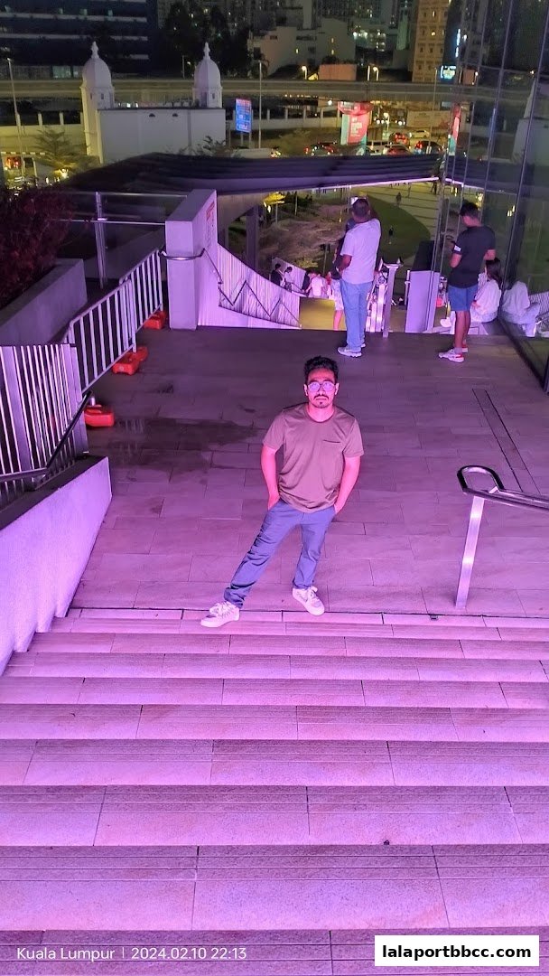 A man poses on illuminated steps with a city skyline in the background at night.
