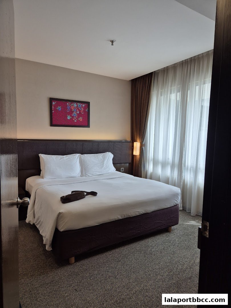 A hotel room with a king-size bed, bedside table, and a window with curtains.