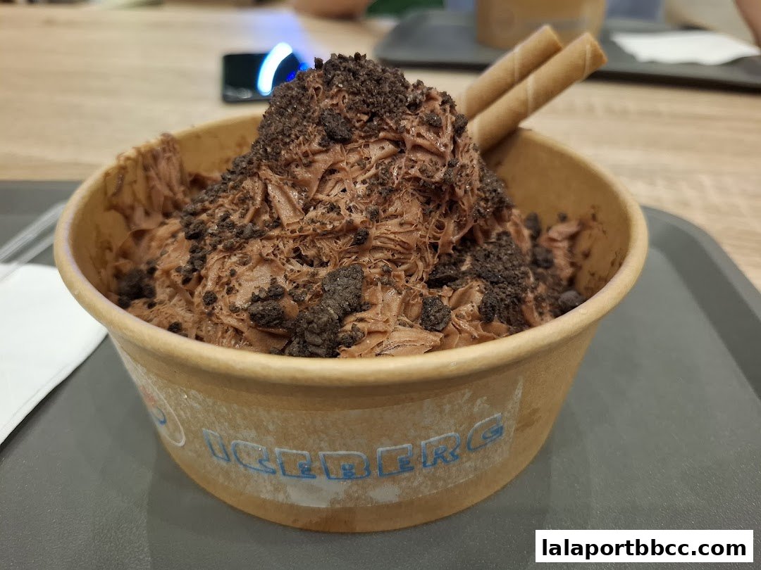 A close-up of a chocolate shaved ice dessert topped with cookie crumbles and wafer sticks.