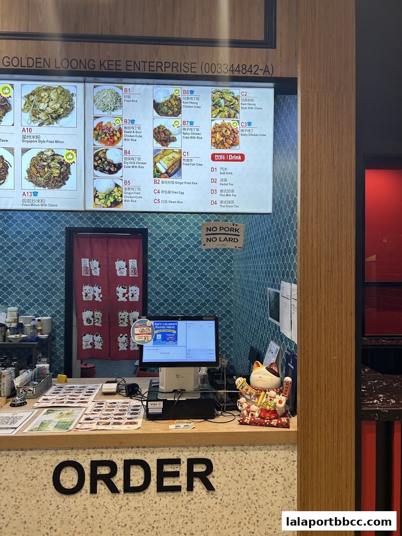 A food stall counter with a digital menu board displaying various dishes and drinks.