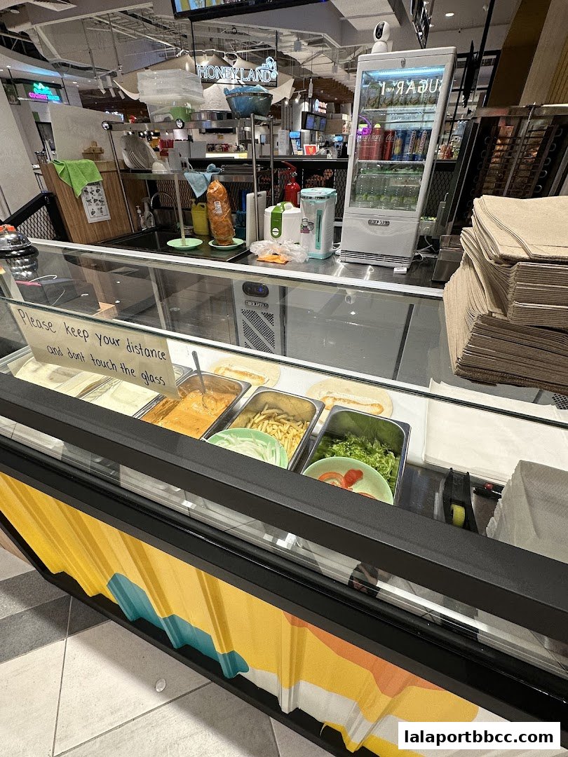 A food counter with various ingredients for kebabs and a refrigerated display of drinks.