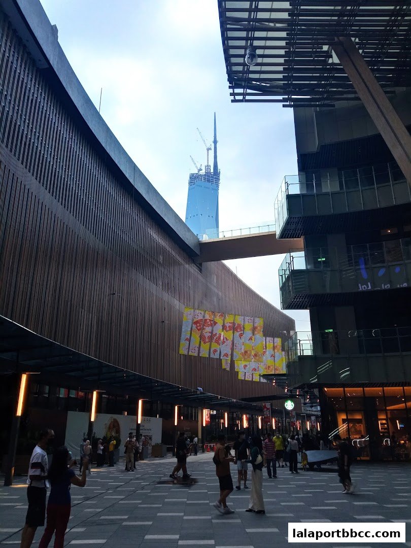 People walking in a modern plaza with a tall building under construction in the background.
