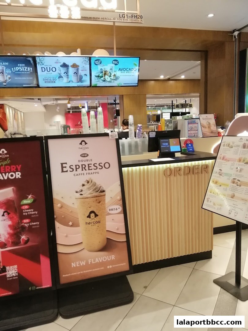 A beverage shop counter with digital menu boards and promotional posters.