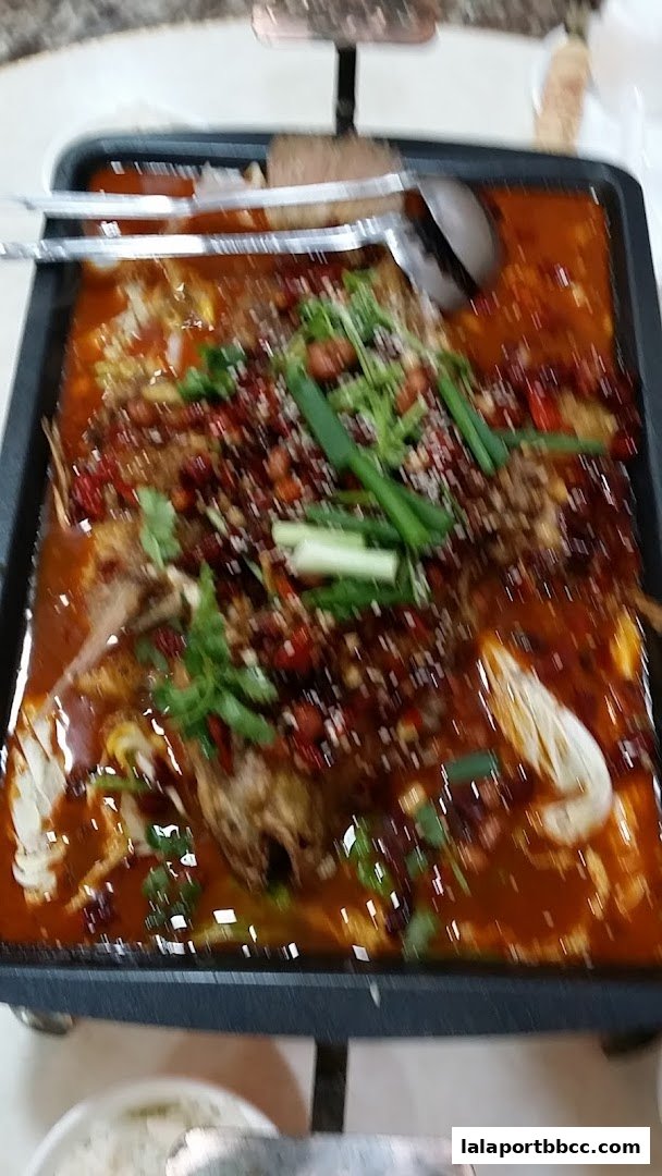 A close-up of a spicy fish dish served in a black tray with chili peppers and herbs.