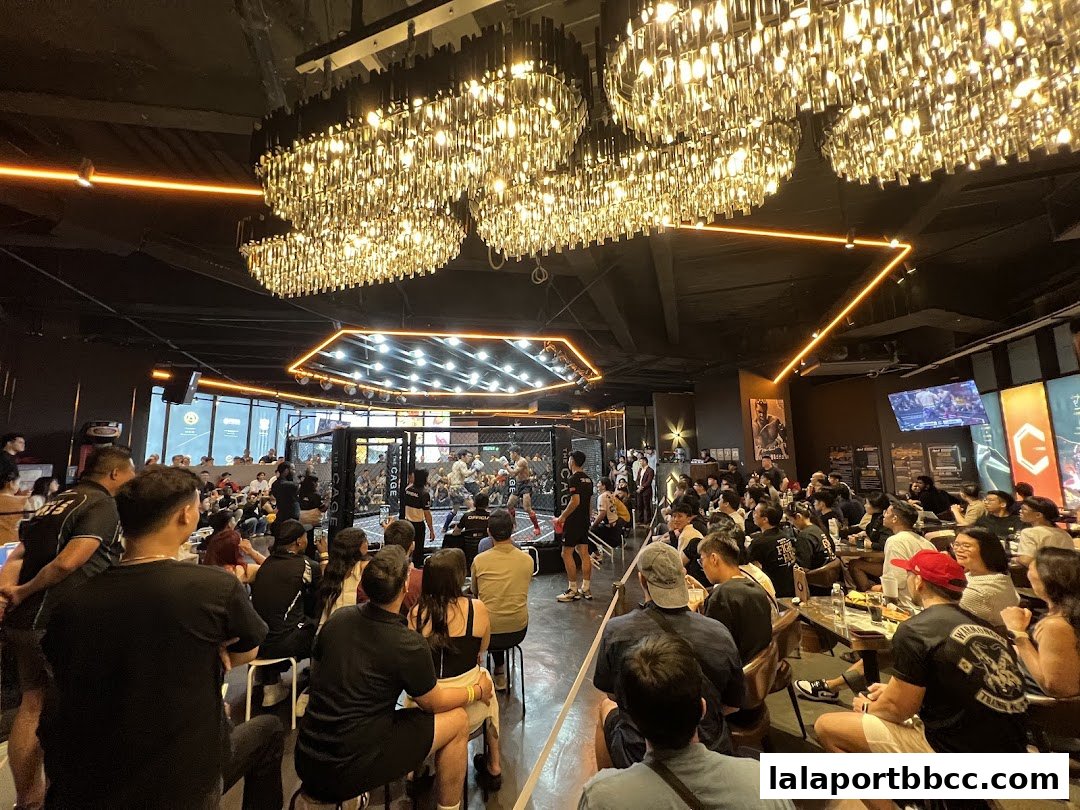 A lively indoor venue with a boxing ring, audience, and stylish chandeliers.