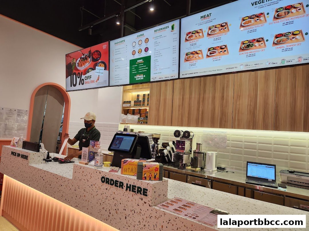 A cashier stands behind a counter with digital menus displaying food items and promotions.
