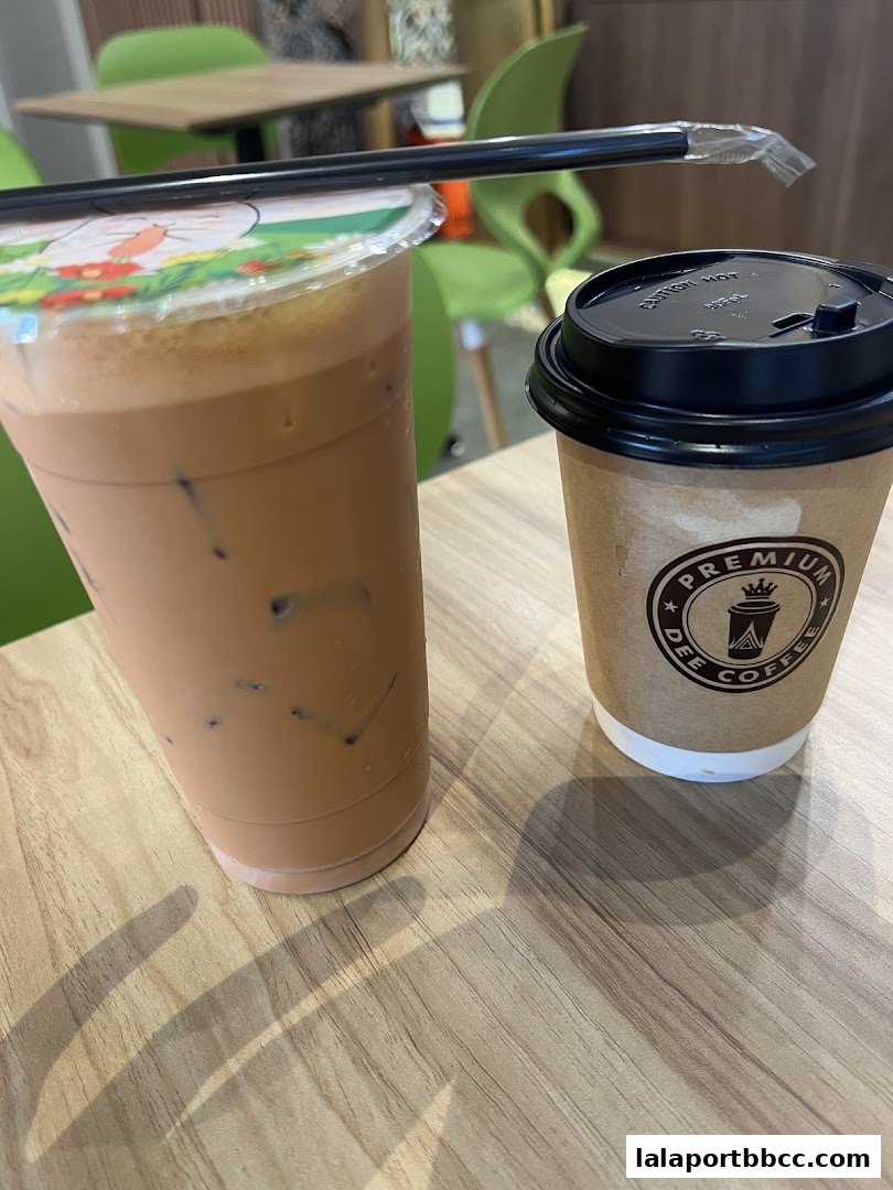 Two drinks, one in a plastic cup with a straw and another in a paper cup, sit on a wooden table.