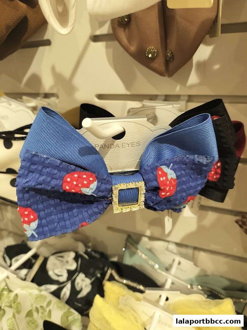 A close-up of a blue bow with a strawberry pattern and a jeweled center.