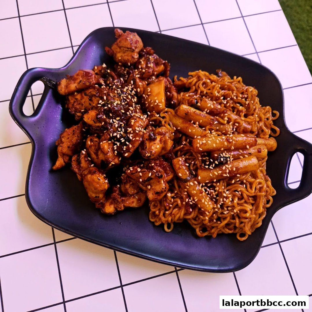 A black platter holds a serving of Korean fried chicken and tteokbokki with ramen noodles.