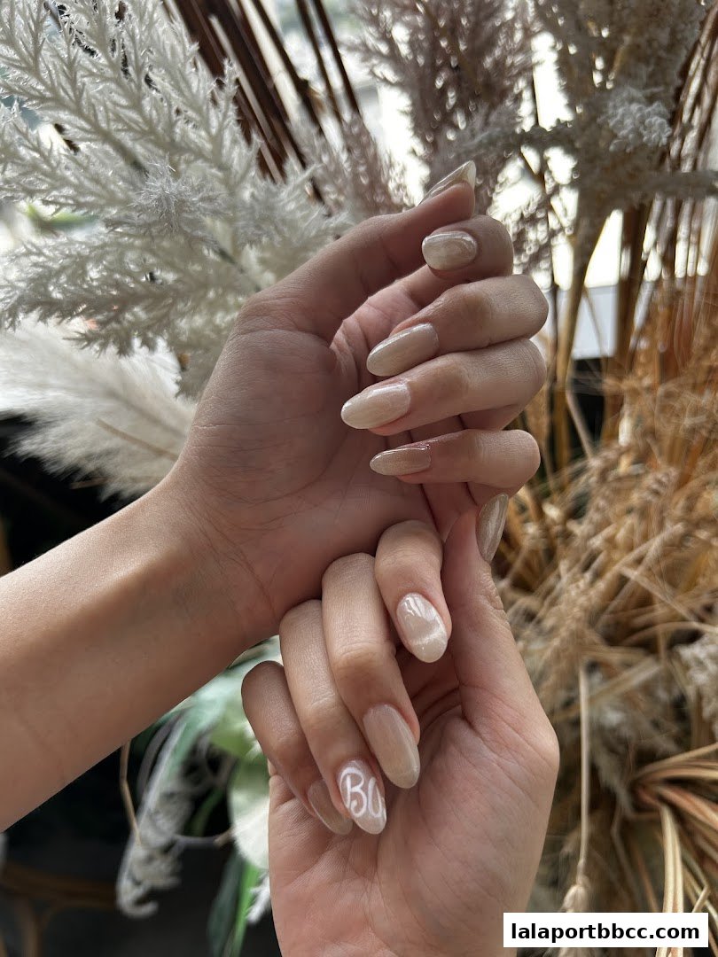 Close-up of hands with beautifully manicured nails, featuring a subtle pearlescent finish and delicate white lettering.