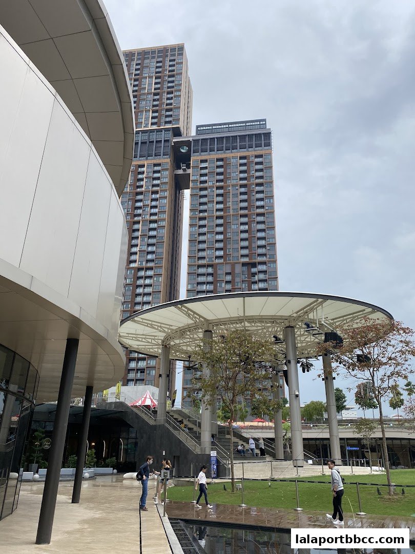 People walking in an outdoor plaza with modern architecture and tall buildings in the background.
