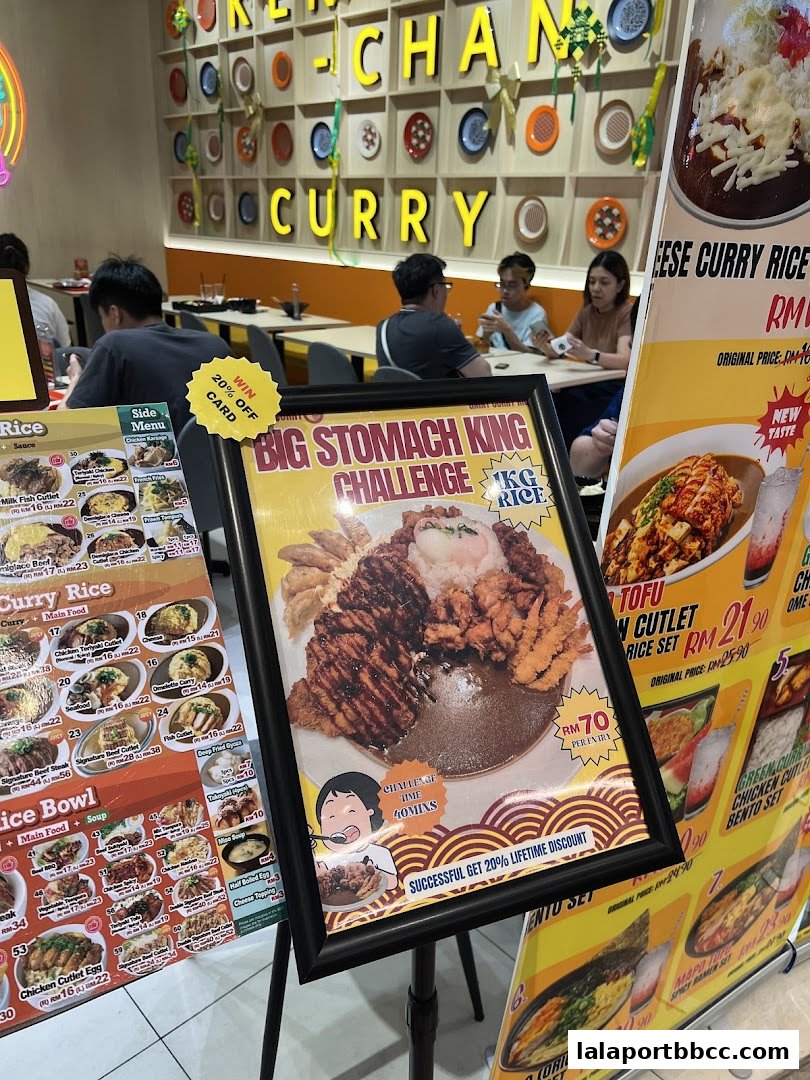 A restaurant interior with customers dining and promotional posters for curry dishes and a food challenge.
