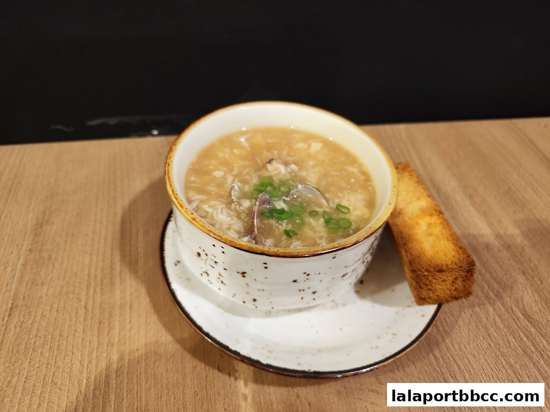 A steaming bowl of crab soup with chopped green onions and a piece of toast.