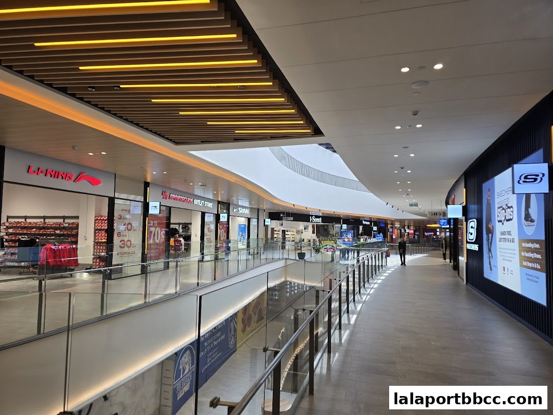 A modern shopping mall interior with various retail stores and a long walkway.