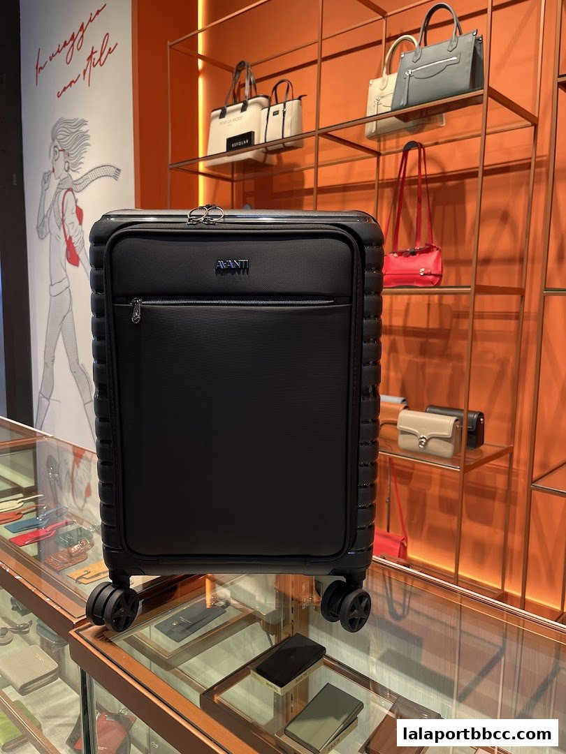 A black suitcase is displayed in a store with handbags and accessories on shelves.
