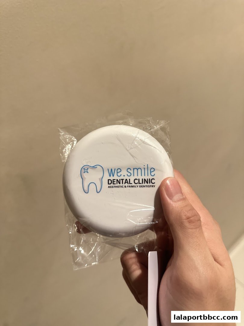 A hand holds a small, round, white dental product with the WeSmile Dental Clinic logo.