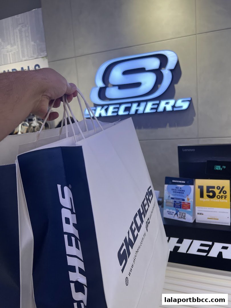 A hand holds shopping bags in front of a Skechers store logo and a 15% off sign.