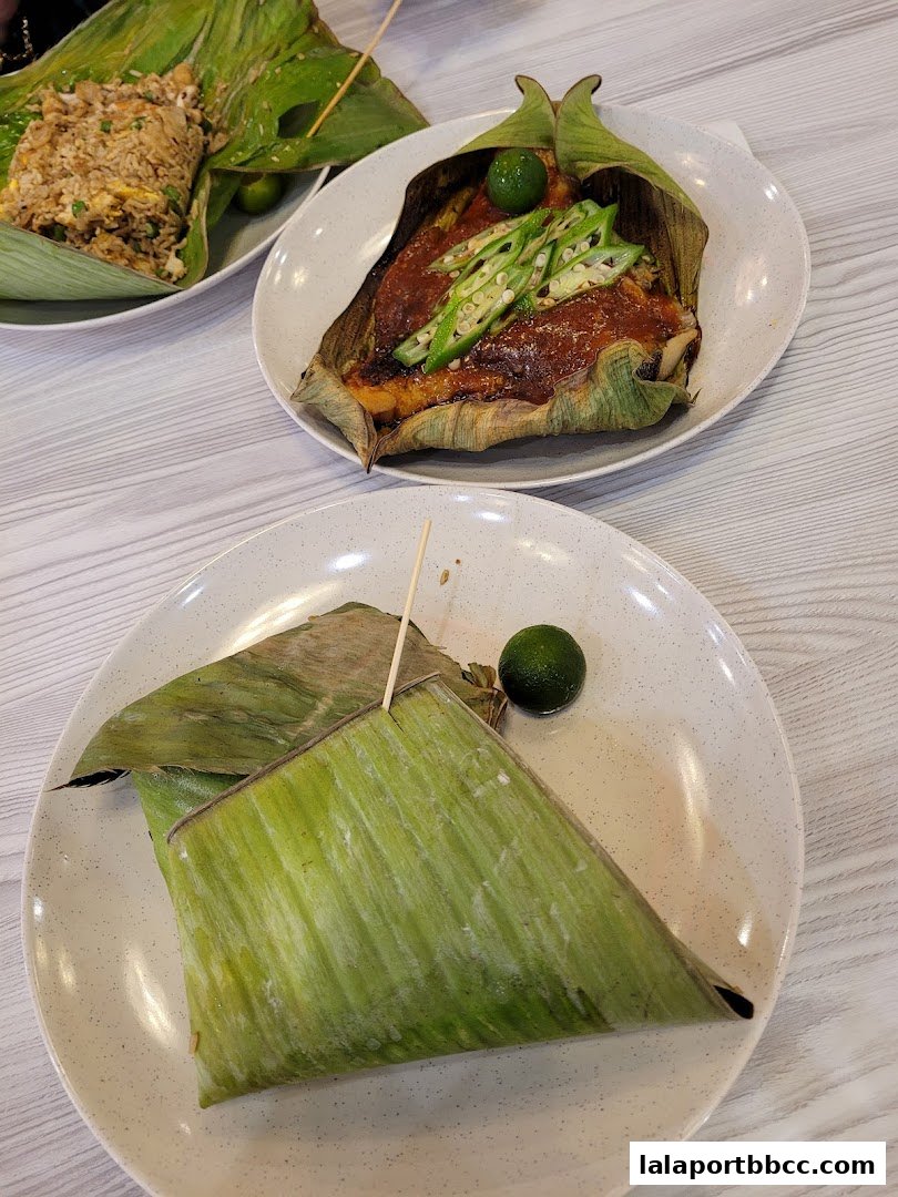 Two plates of food, one with grilled fish and okra, the other with fried rice, both wrapped in banana leaves.