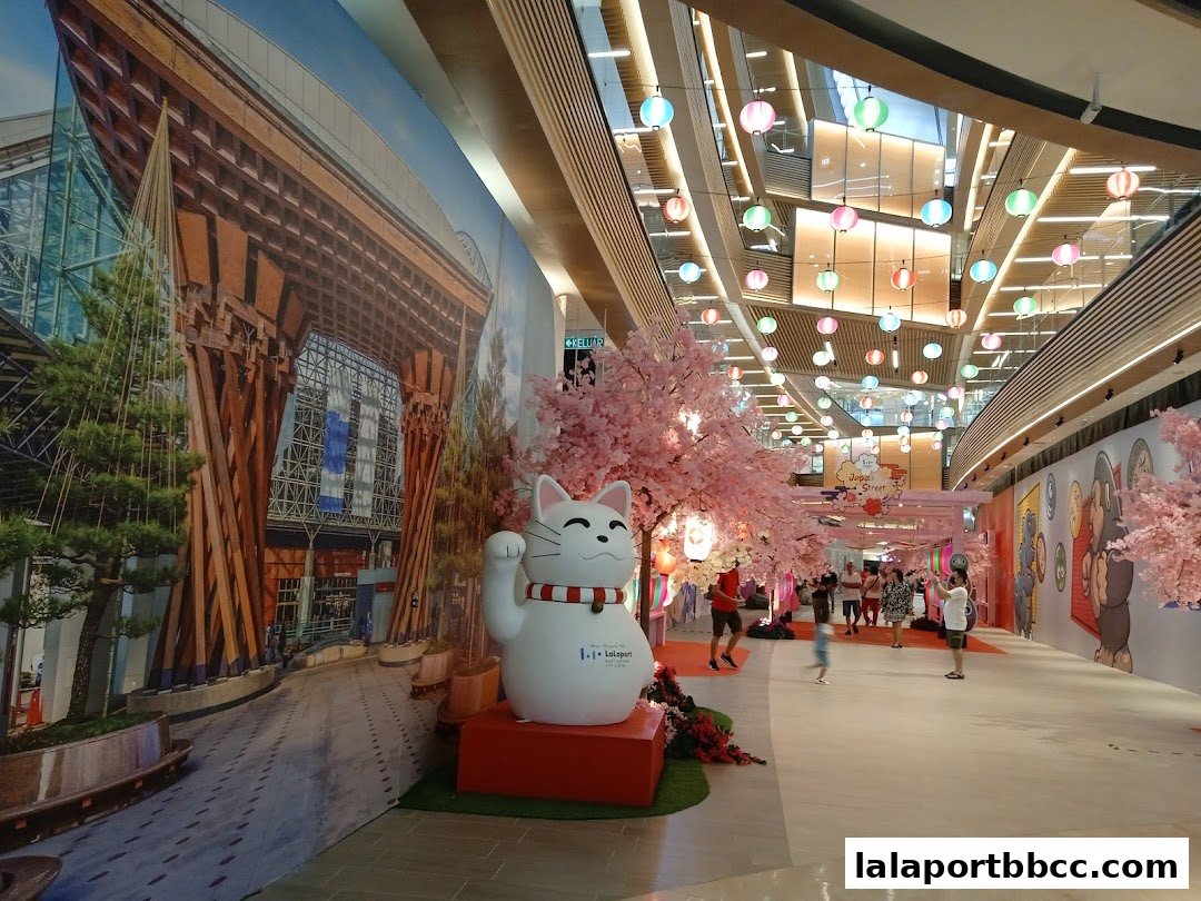 A festive mall interior decorated with cherry blossoms and a large Maneki-neko cat.