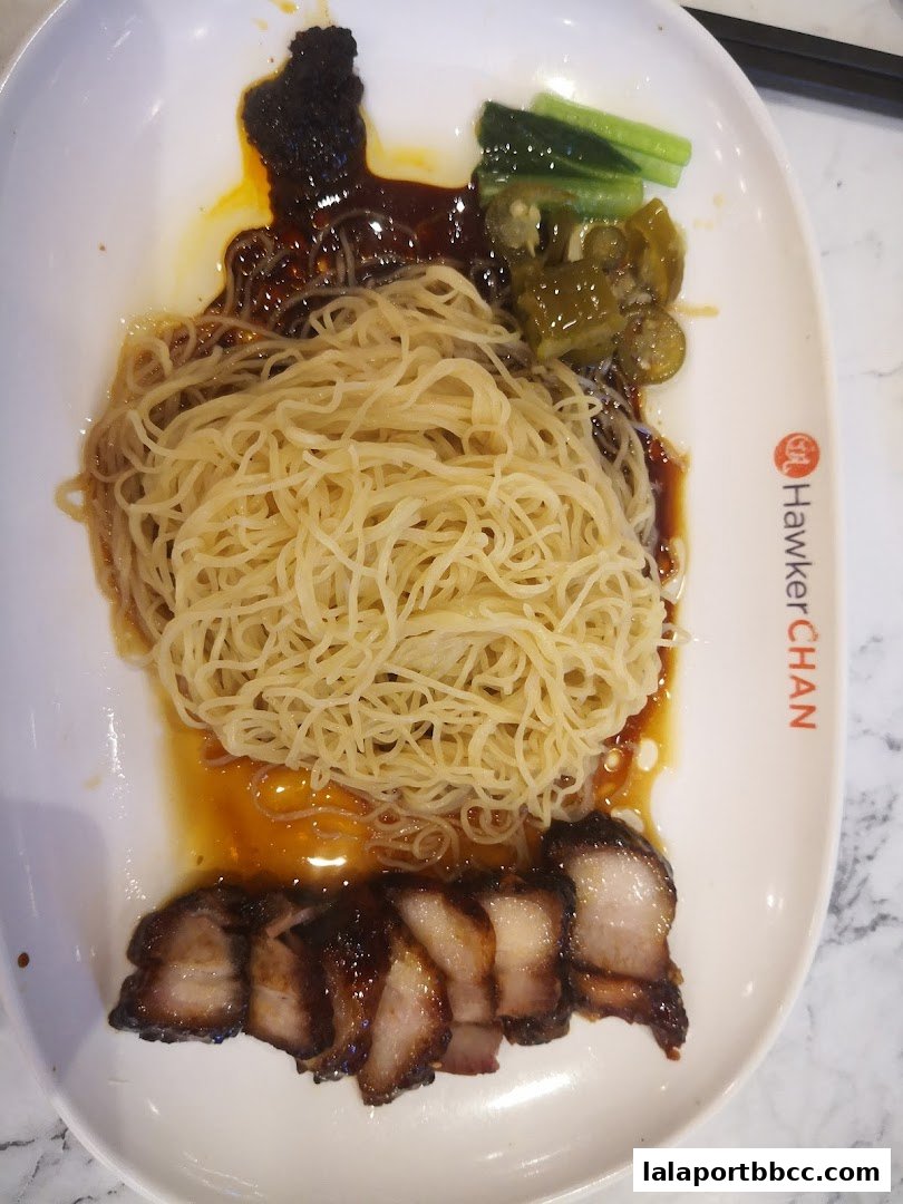 A plate of char siew noodles with pickled vegetables and chili paste.