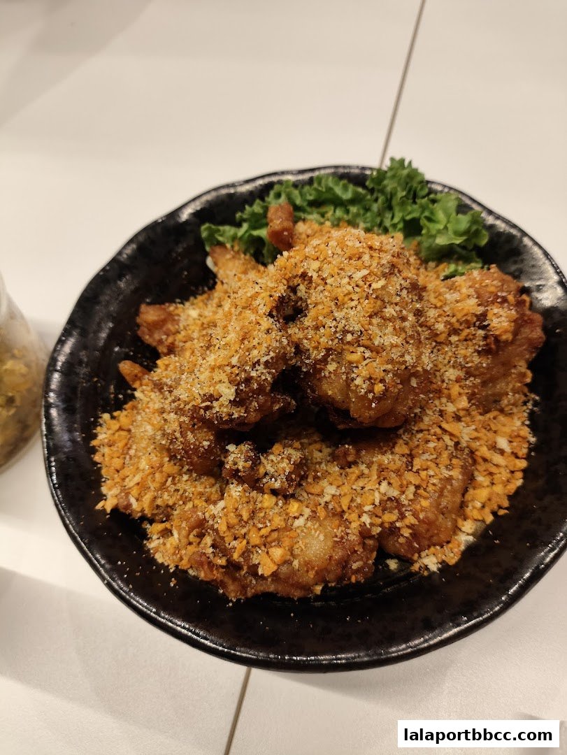 A close-up shot of a black bowl filled with crispy fried chicken pieces topped with crunchy crumbs and garnished with lettuce.