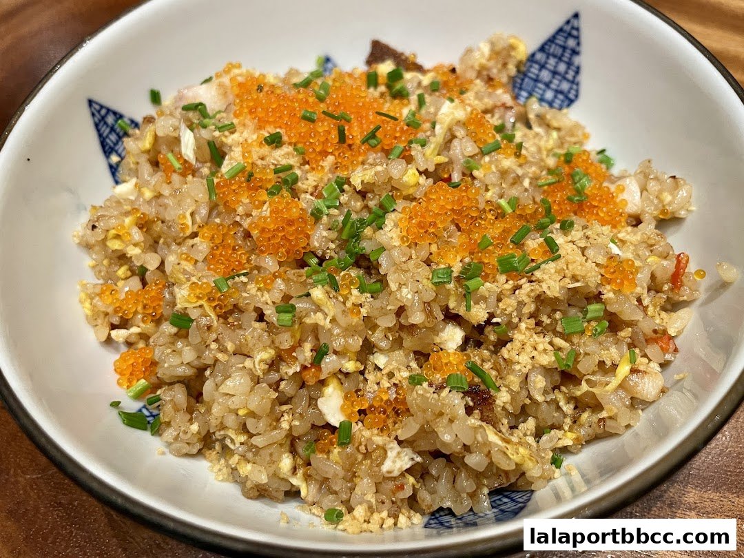 A close-up shot of a bowl of fried rice topped with tobiko and chopped scallions.