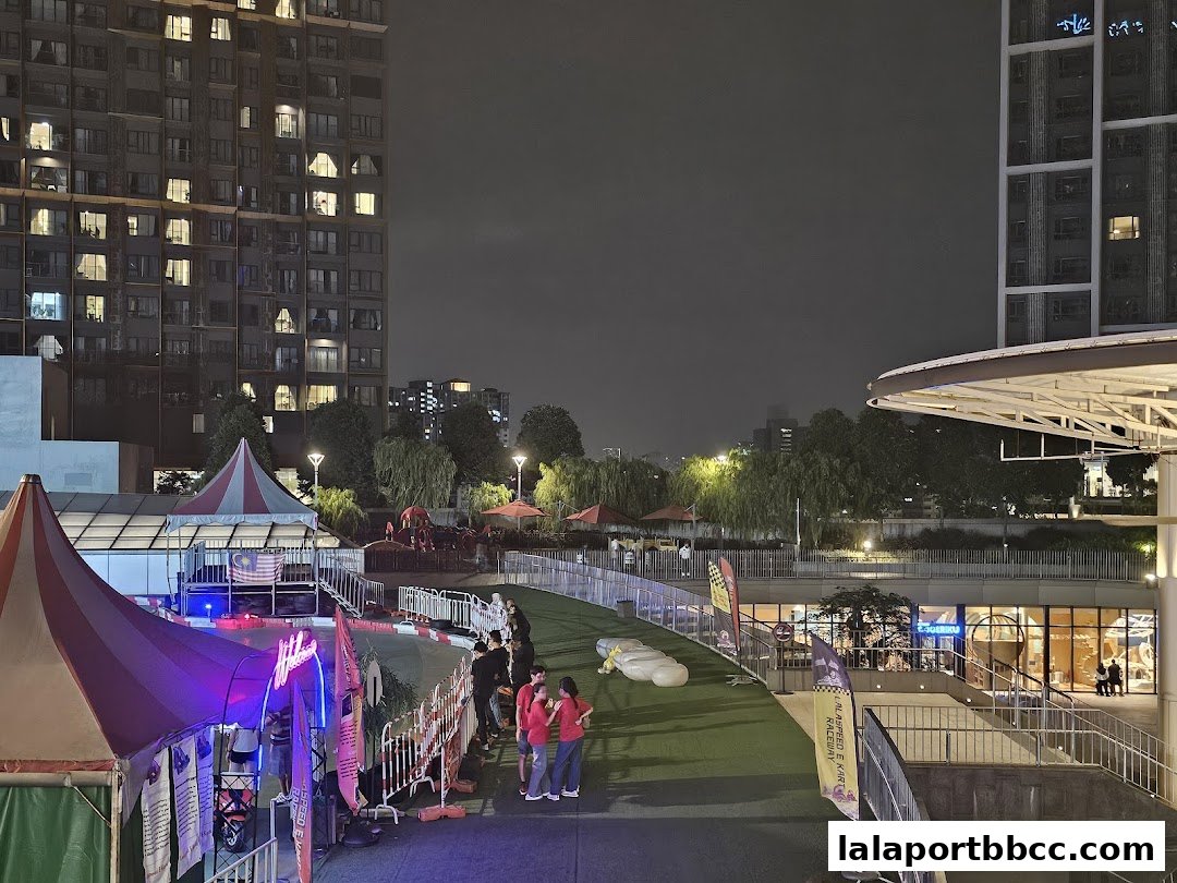 Night view of an outdoor go-kart raceway with tents and surrounding buildings.