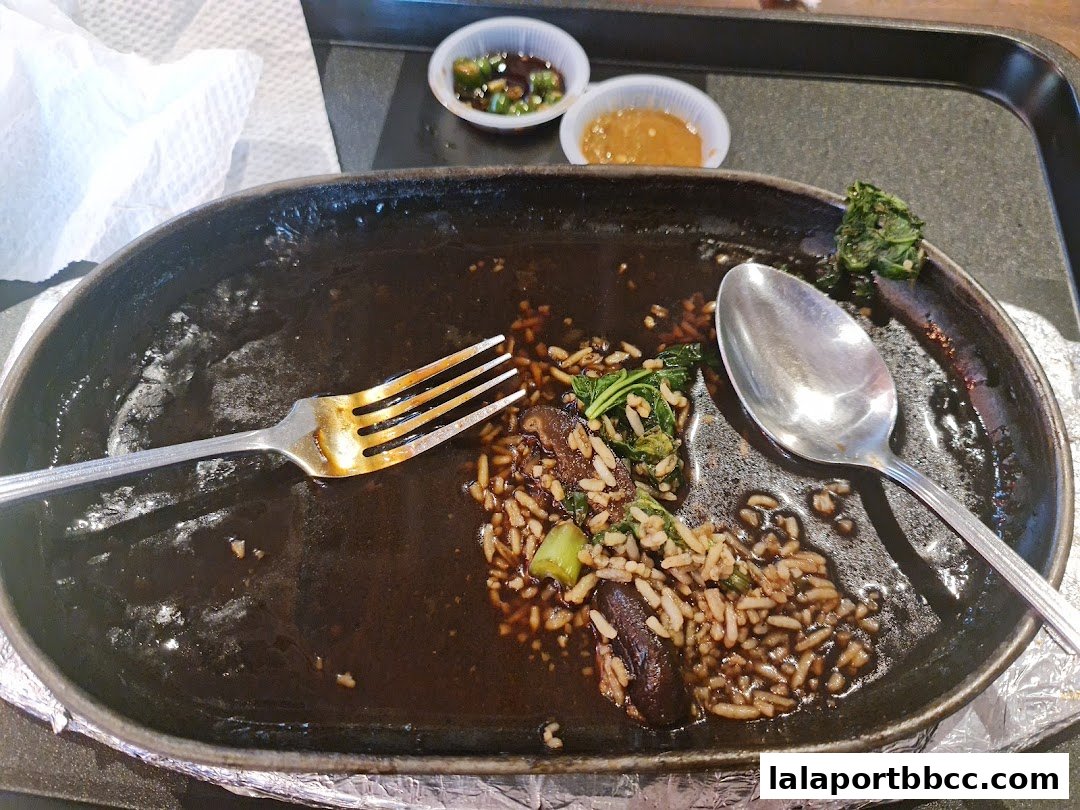 A sizzling plate with rice, vegetables, and mushrooms, partially eaten, with cutlery and dipping sauces.