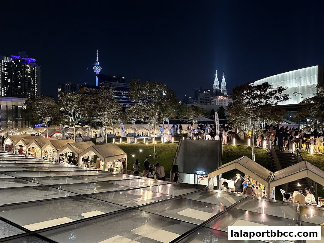 A lively night market with numerous stalls set up on a grassy slope, illuminated by lights.