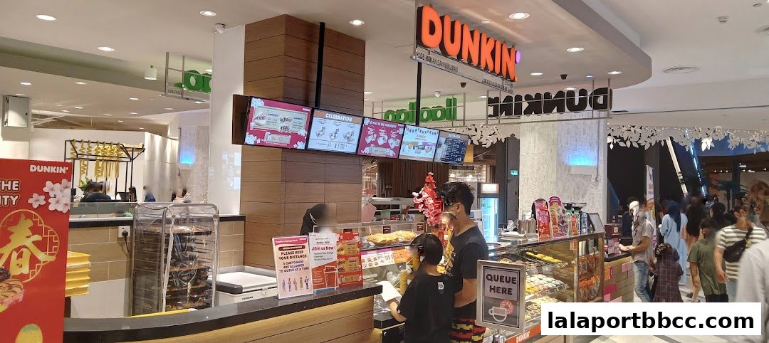 A busy Dunkin' Donuts store with customers ordering and displays of donuts and beverages.
