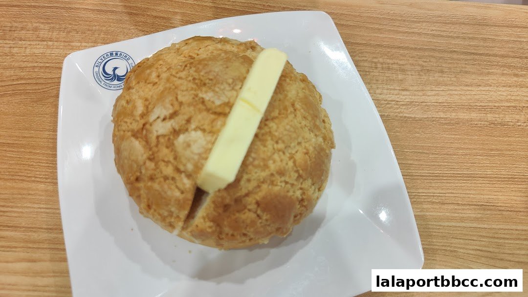 A close-up of a pineapple bun with butter on a white plate.
