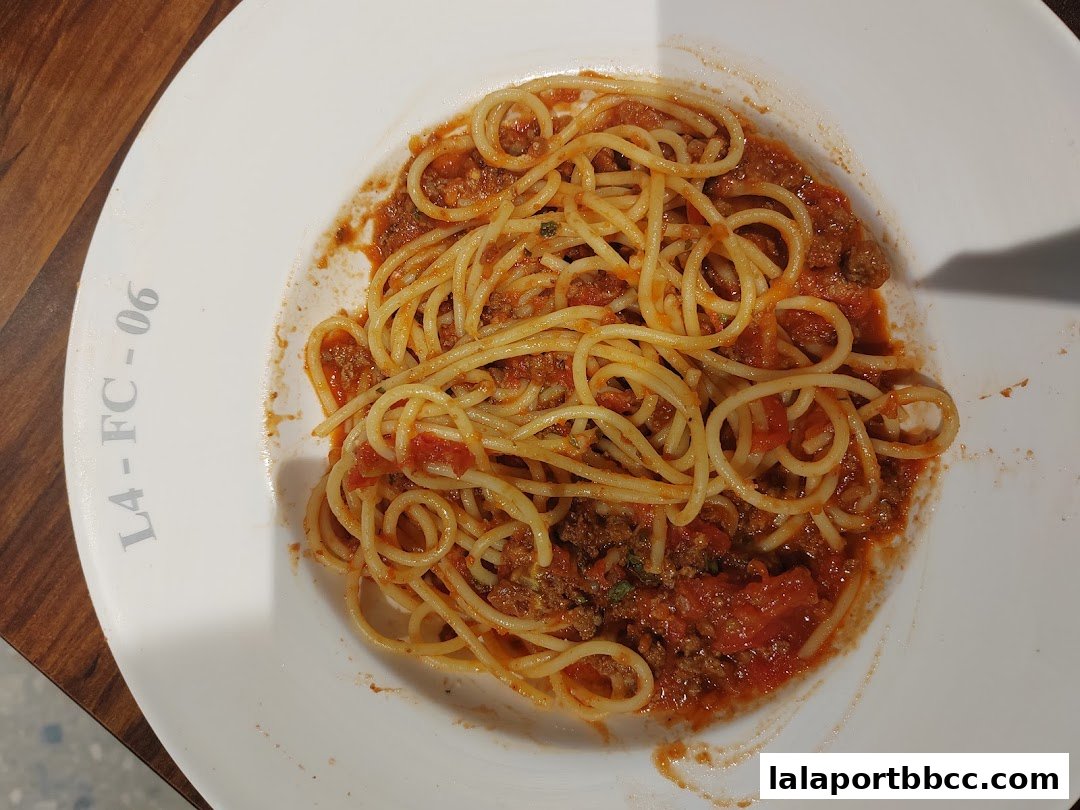 A plate of spaghetti bolognese served in a white bowl on a wooden table.
