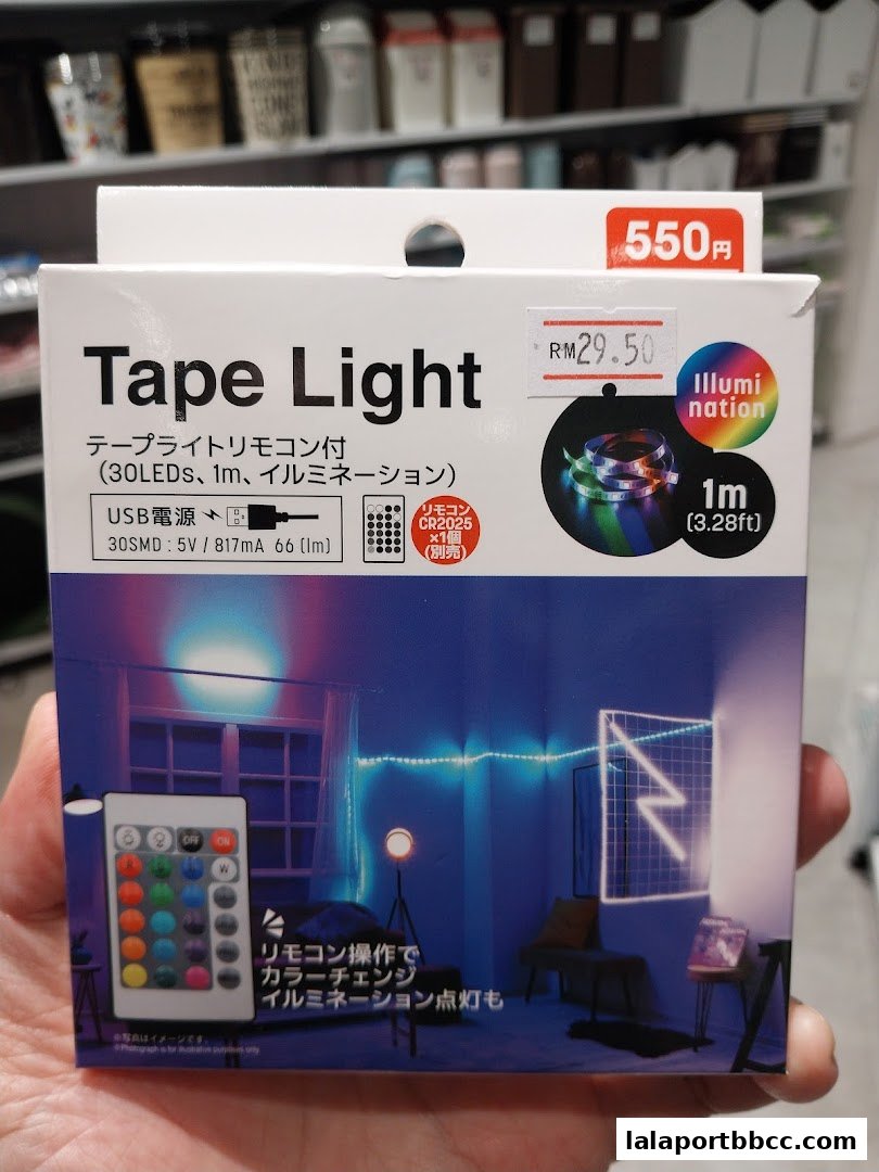 A hand holds a box for a DAISO Tape Light with a remote control.
