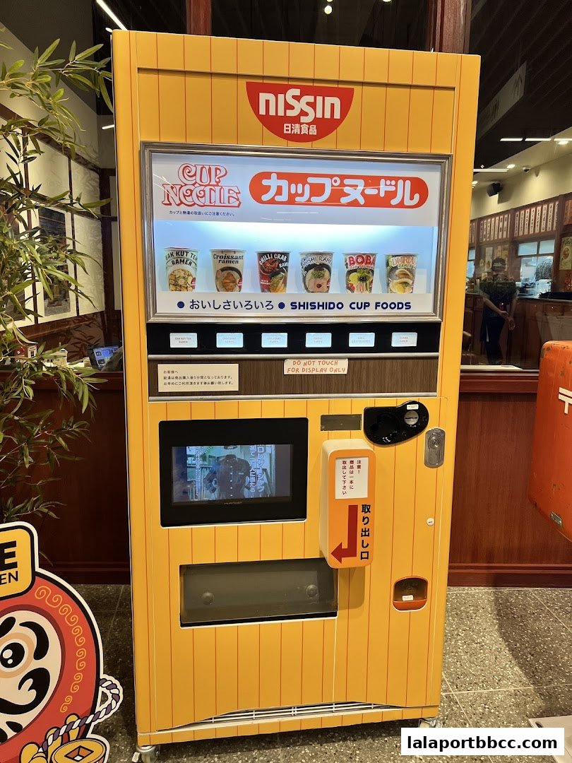 A bright yellow vending machine offering various Nissin Cup Noodles.