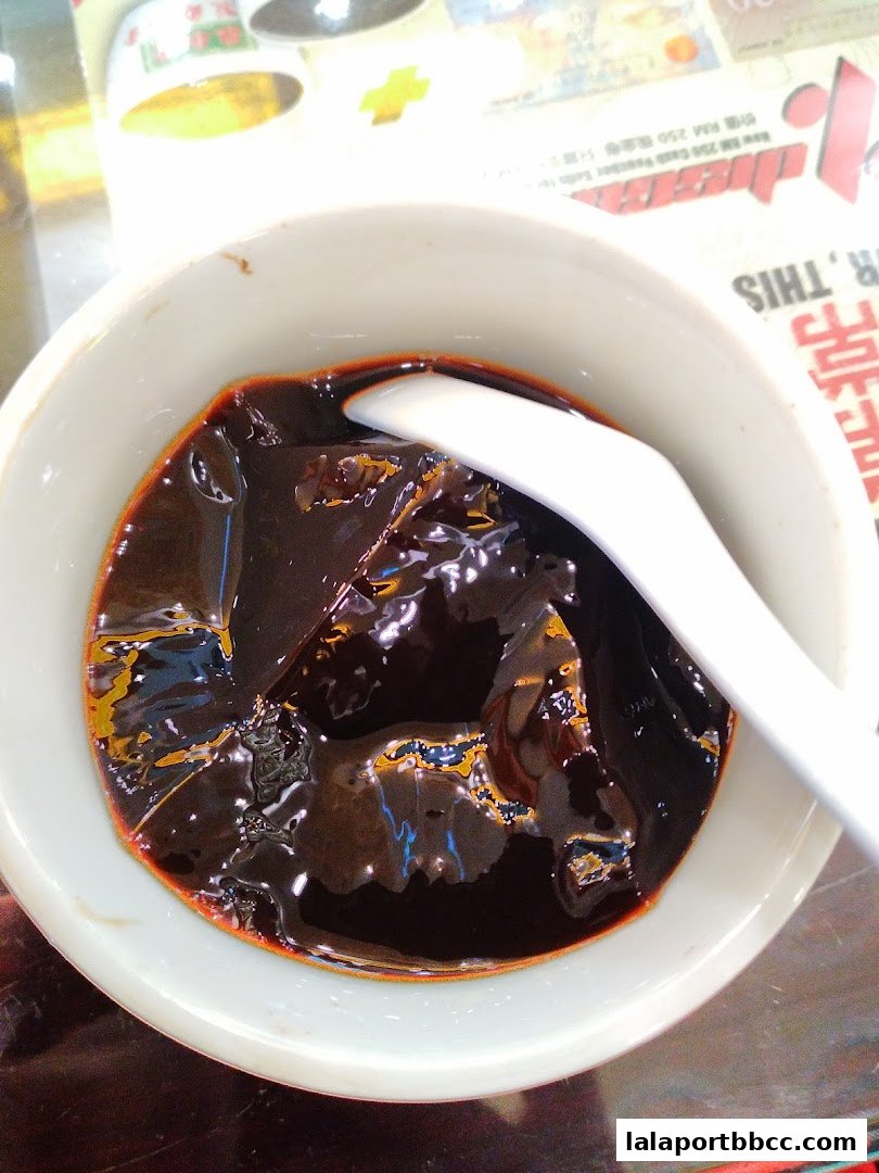A close-up shot of a bowl of dark herbal jelly with a white spoon.