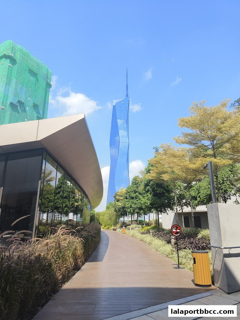 A pathway leads past a modern building towards a striking blue skyscraper.