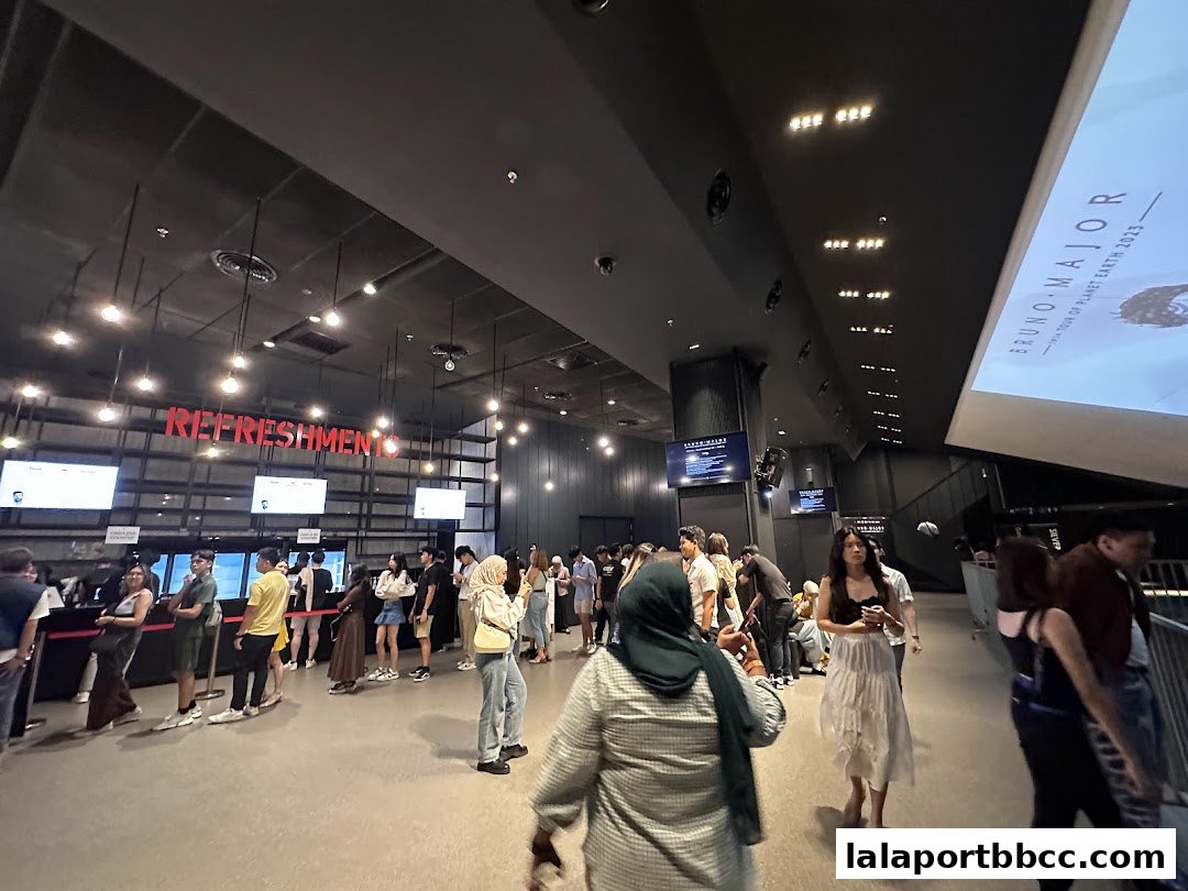 People queuing at a refreshments counter inside Zepp Kuala Lumpur with a concert poster visible.