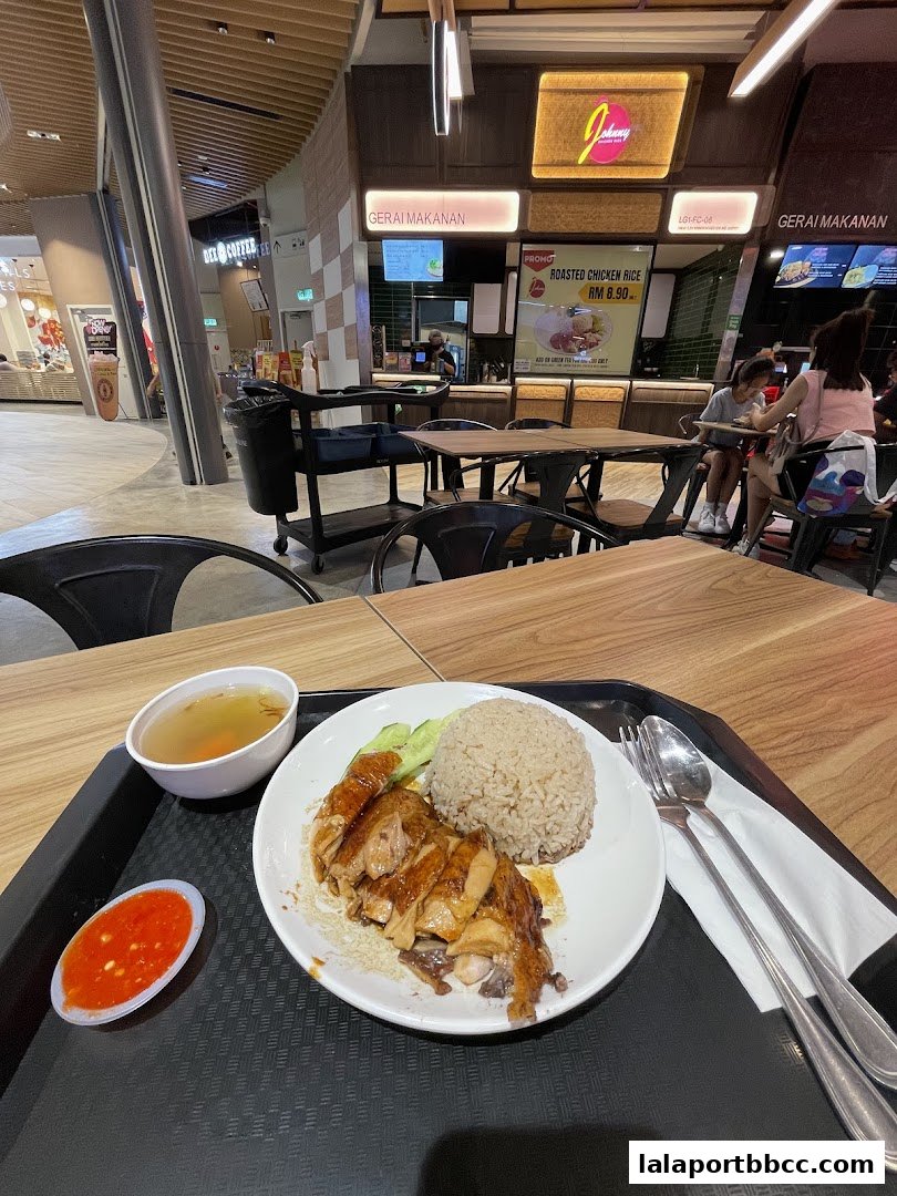 A plate of roasted chicken rice with soup and chili sauce on a tray.