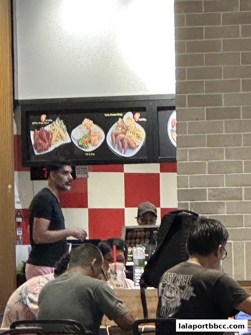 People dining at tables in a restaurant with food images displayed on the wall.