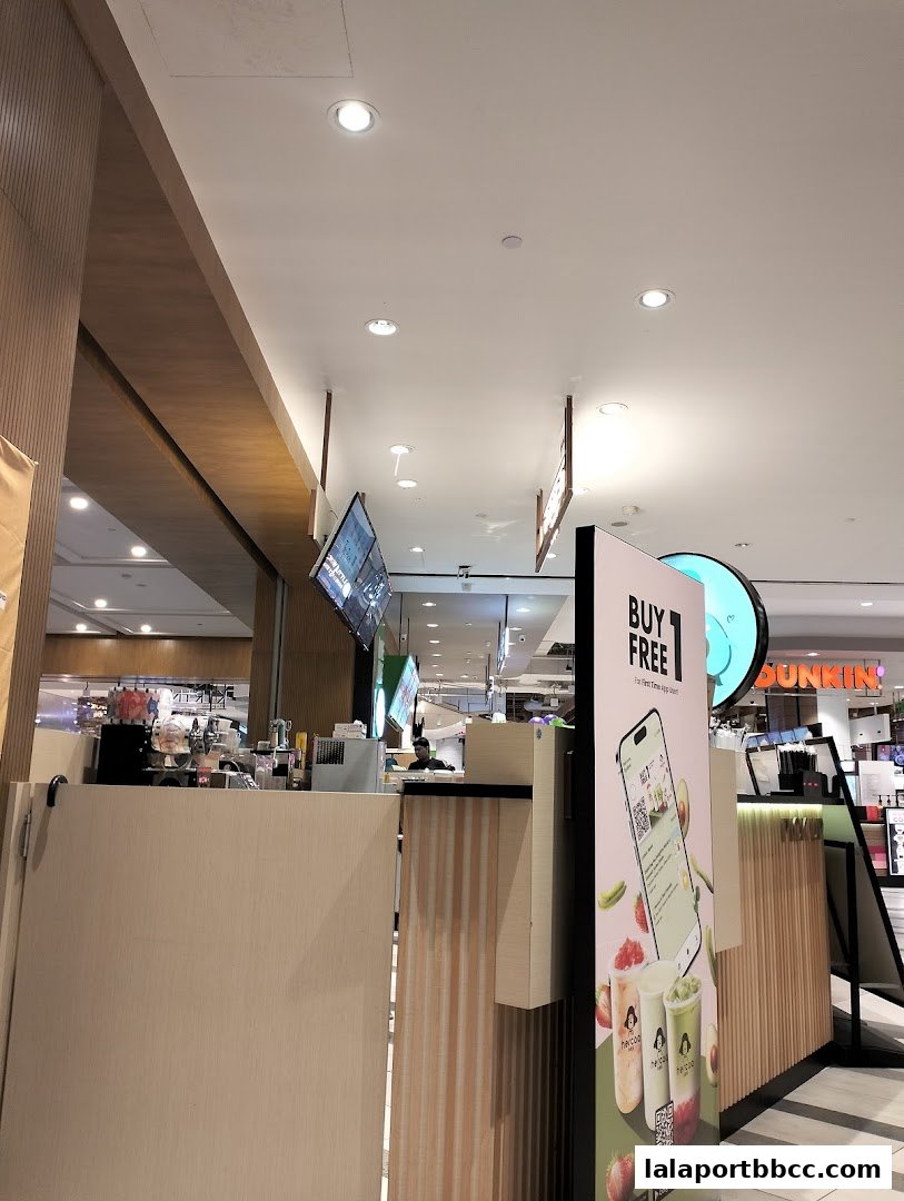 A beverage shop counter with promotional posters and a view of other stores in the background.