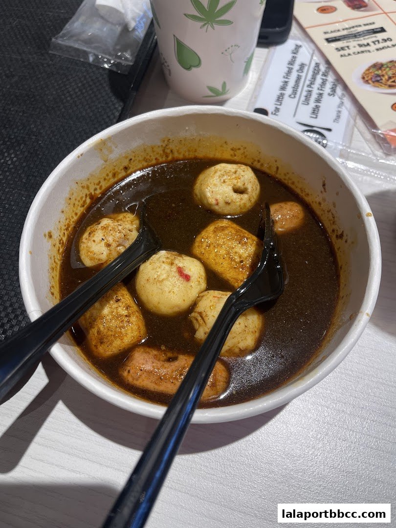 A bowl of savory soup with fish balls and sausage, served with forks.