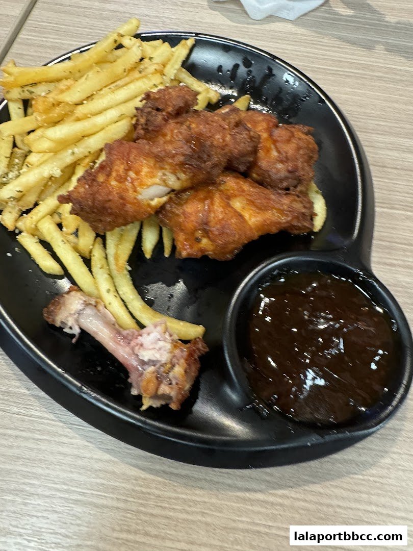 A plate of crispy fried chicken wings and french fries with a side of dipping sauce.