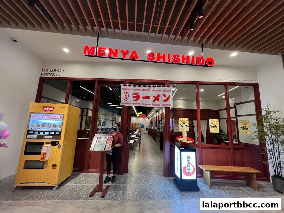 The entrance of Menya Shishido Lalaport BBCC, a ramen restaurant, with a vending machine and seating.