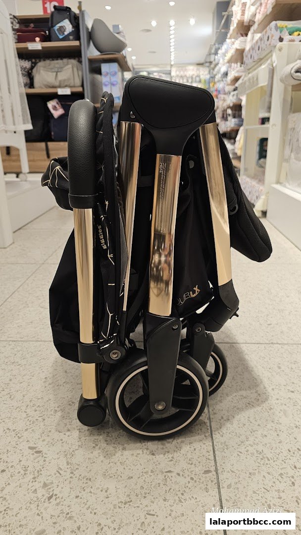 A folded black stroller with gold accents is displayed in a retail store.