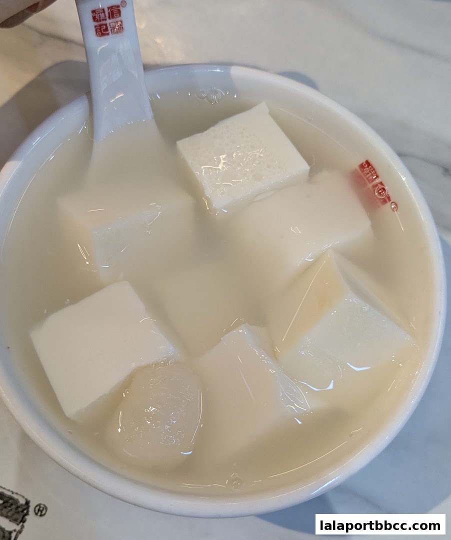 A close-up shot of a refreshing dessert with tofu cubes and lychee in a white bowl.
