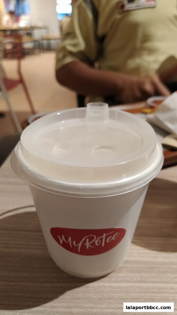 A white cup with a red MyRotee logo and a white lid sits on a wooden table.