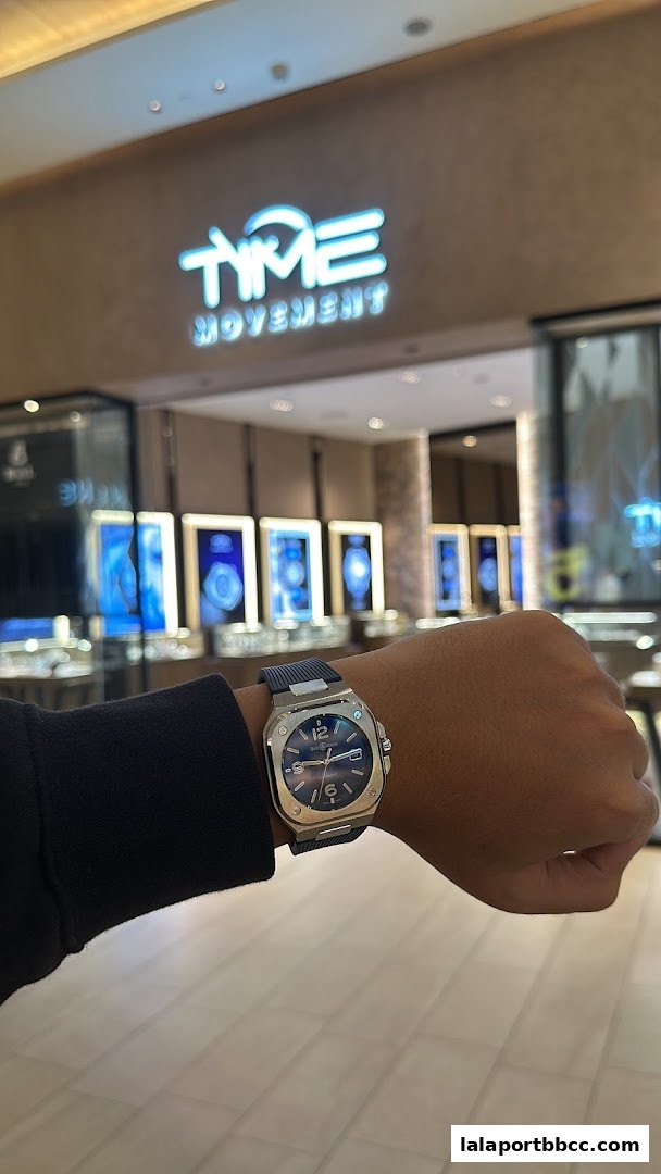 A person wearing a stylish watch in front of the Time Movement shop.