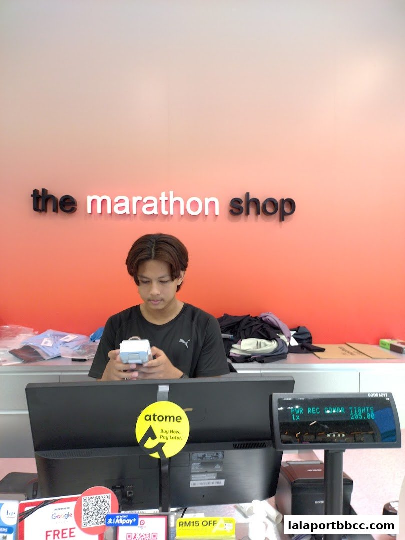 A young man works at the counter of The Marathon Shop, with the store's logo visible.
