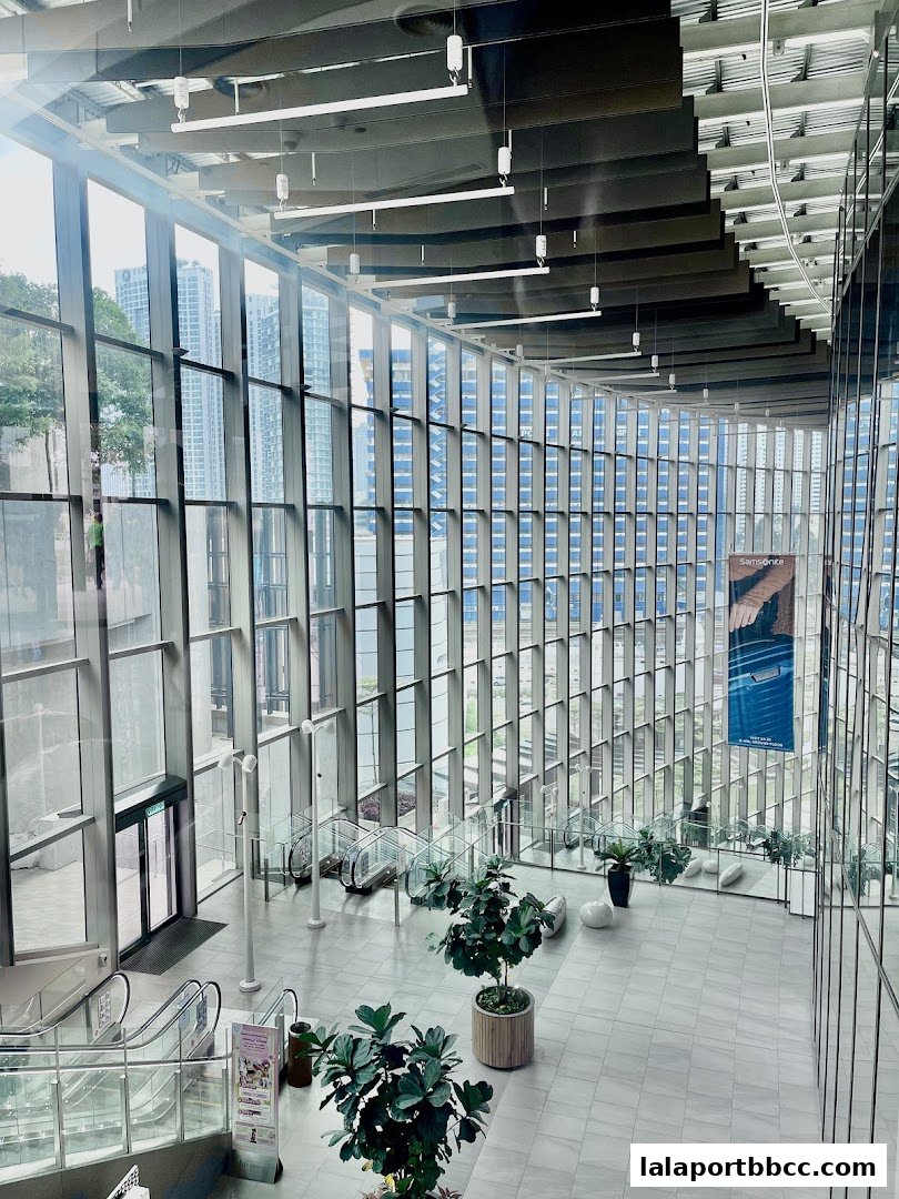 Interior view of a modern shopping mall atrium with escalators and large windows.