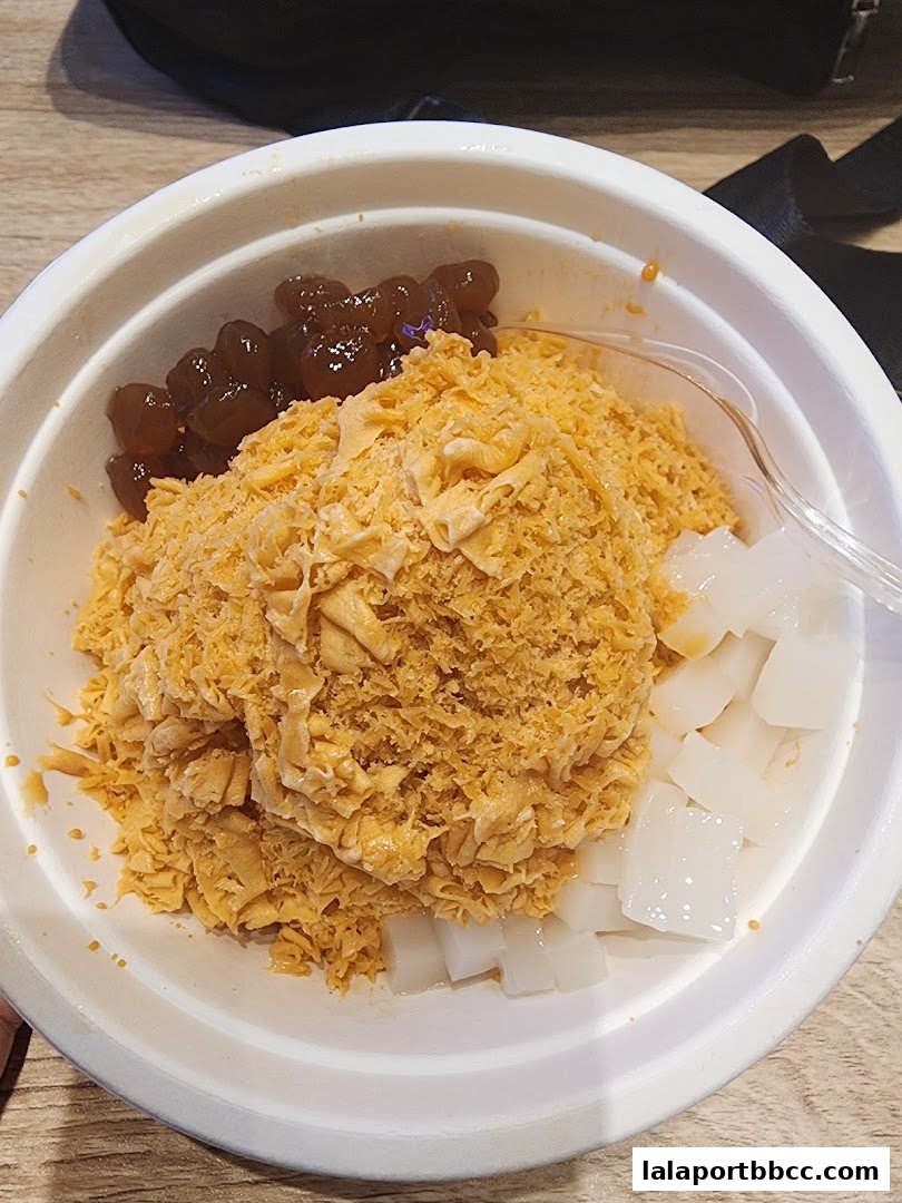 A bowl of shaved ice dessert with toppings of boba pearls and white jelly cubes.